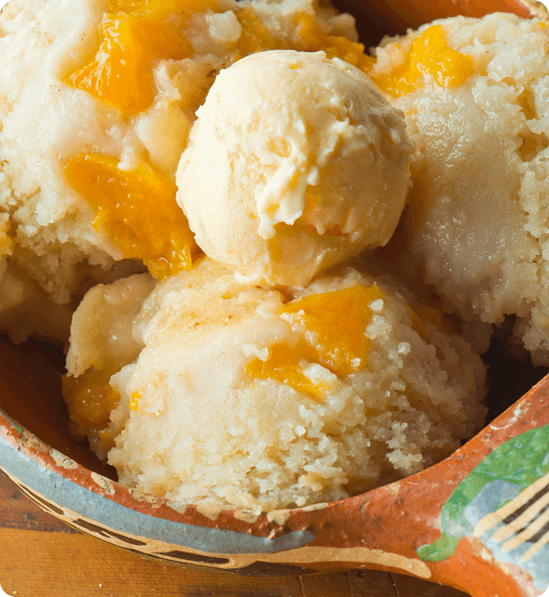 Scoops of creamy yellow-orange ice cream with chunks of fruit in a decorative bowl.